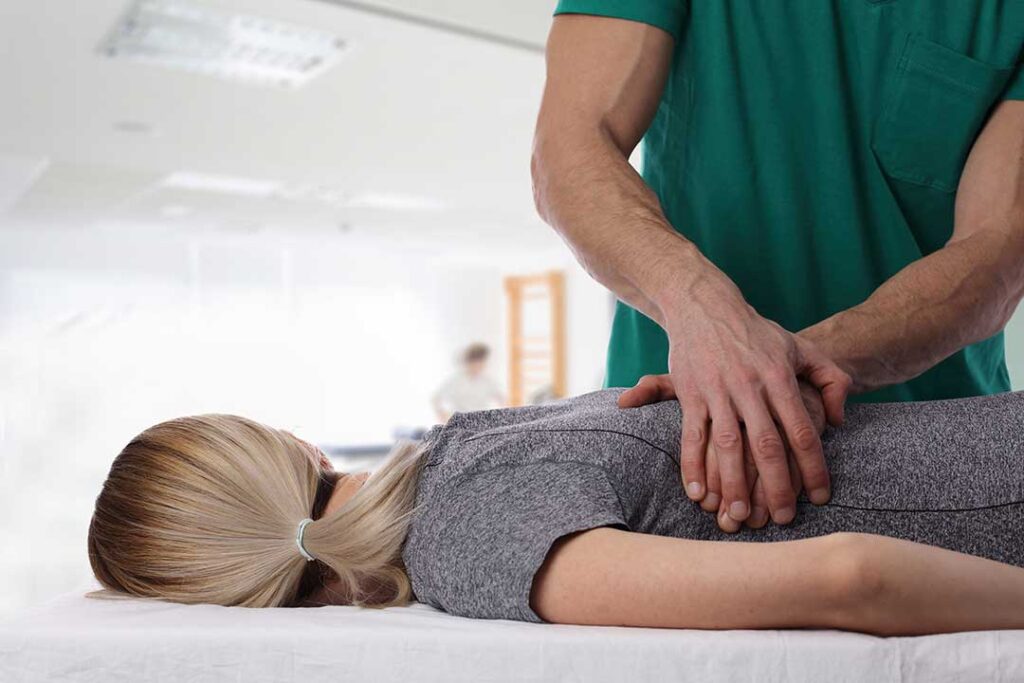Physical therapist guiding a patient through a supervised balance exercise beside a treatment table.