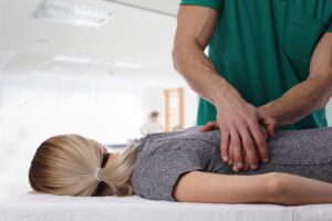 Physical therapist guiding a patient through a supervised balance exercise beside a treatment table.