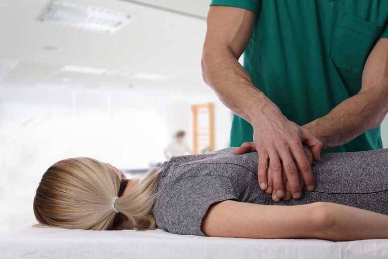Physical therapist guiding a patient through a supervised balance exercise beside a treatment table.