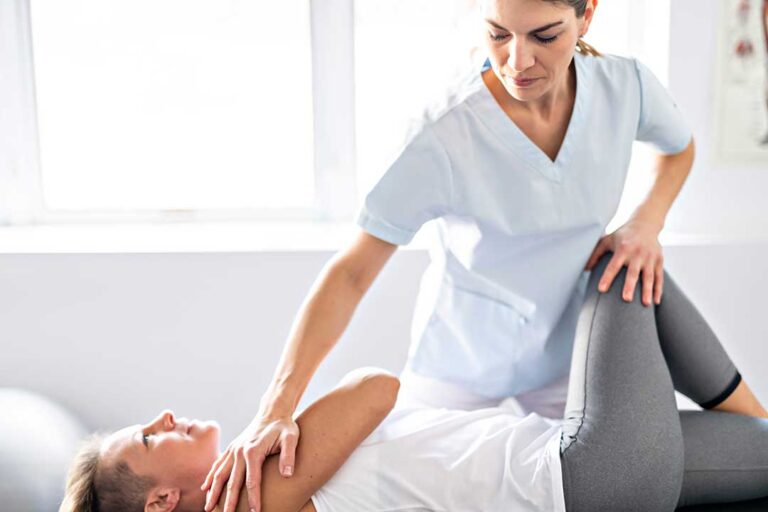 Person resting on a treatment table while gently stretching a sore lower back after an adjustment.